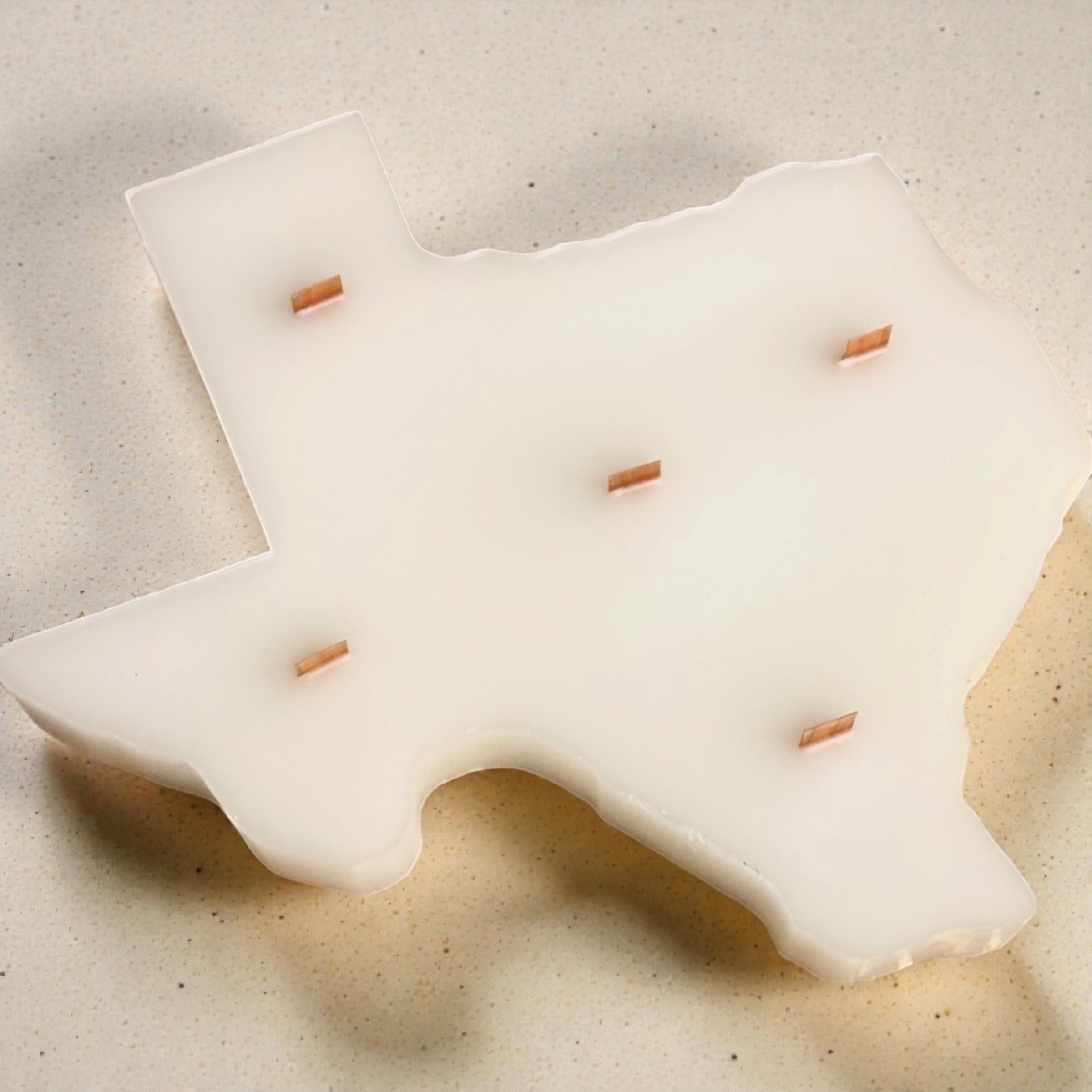 Handcrafted ivory white Texas silhouette paraffin pillar candle with five wood wicks resting on a stone surface. 